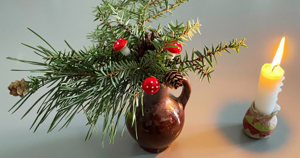 Foto von einer kleinen Vase mit Zweigen und kleinen Glückspilzen und einer kleinen brennenden Kerze.